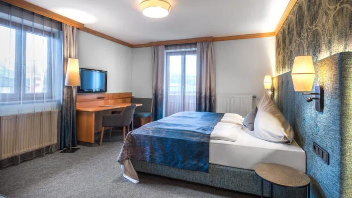 Modernes Hotelzimmer mit Doppelbett, Schreibtisch, Wandfernseher und großen Fenstern mit Bergblick